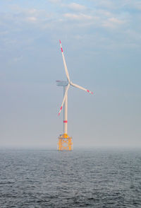 Wind turbine in sea against sky