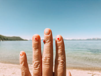 Close-up of hand at sea against clear sky