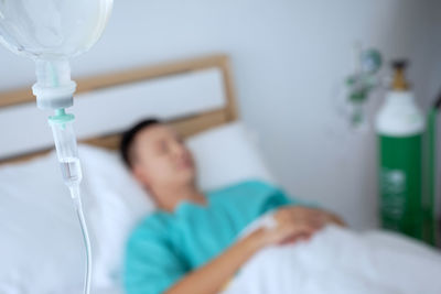 Close-up of iv drip against patient lying on bed in hospital