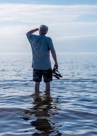  senior male walks in the warm waters of lake michigan, with his sandals in his hand