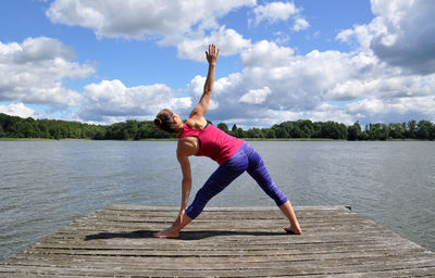 Rear view full length of young woman doing yoga on jetty by lake