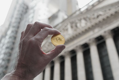 Low angle view of hand holding bitcoin against building