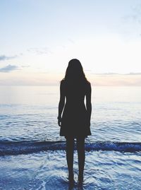 Rear view of silhouette woman standing at beach against sky