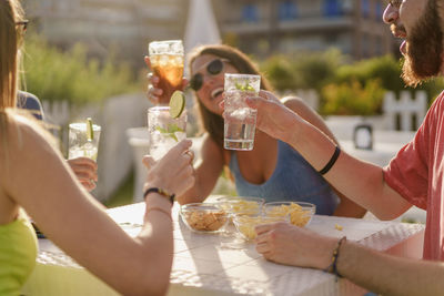 Young friends clinking with fresh mojitos sitting and taking aperitif in the summer