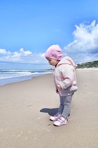 Side view of cute girl wearing warm clothing at beach against sky