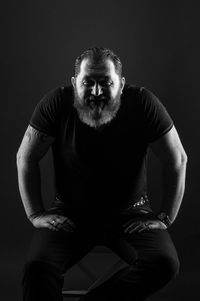 Portrait of young man sitting against black background