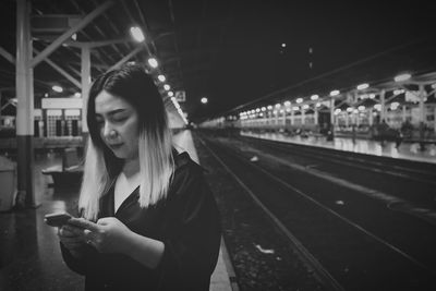 Woman using phone at railroad station platform during night