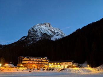 Illuminated building against snowcapped mountains at night