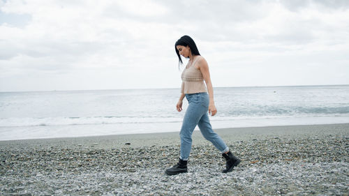 Side view of woman standing at beach against sky