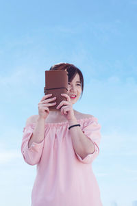 Happy woman holding purse against blue sky