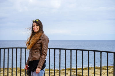 Portrait of smiling young woman standing by railing against sea