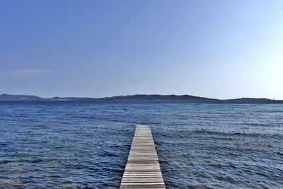 Pier over sea against clear blue sky