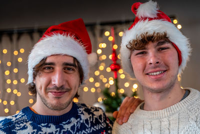 Portrait of two smiling young men wearing red hat in front of a wall of christmas lights