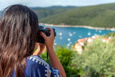 Rear view photo of woman using professional dslr camera, standing on balcony overlooking bay of sea