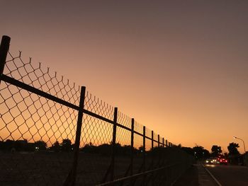 Silhouette fence by road against sky during sunset