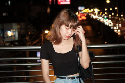 Young woman with hand in hair standing outdoors at night