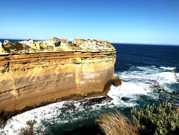 Rock formations by sea against clear blue sky