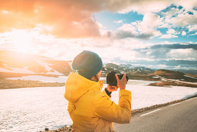 Side view of woman photographing with camera while standing on snow