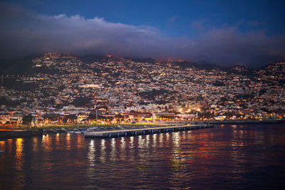 Illuminated city by river against sky at night