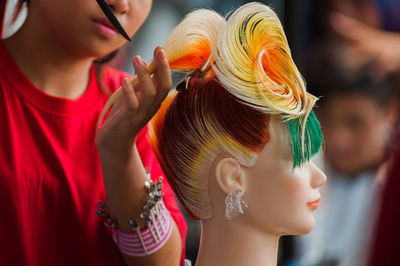 Young woman combing wig of mannequin