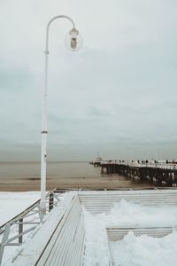 Snow covered street by pier against sky