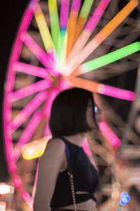 Woman standing by illuminated ferris wheel at night