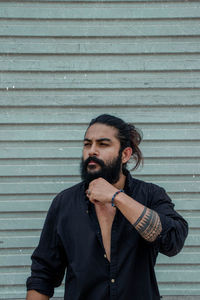 Young man looking away while standing against wall