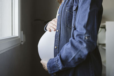 Pregnant woman touching belly by window at home