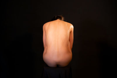 Rear view of naked woman against black background