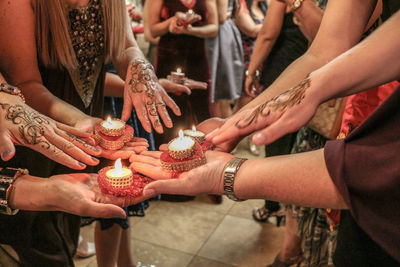 Female friends holding lit tea light candles while showing henna tattoos during ceremony