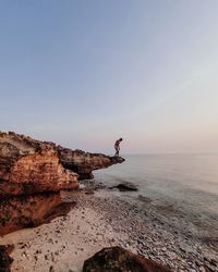 Man on rock by sea against sky during sunset