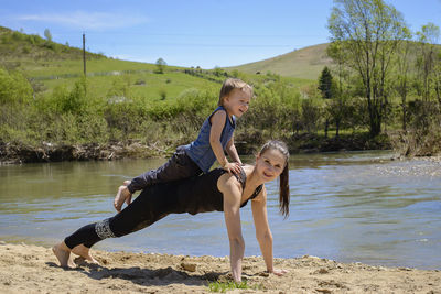 Full length portrait of mother exercising with son by river during sunny day