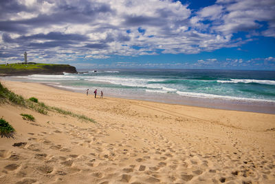 People at beach against cloudy sky