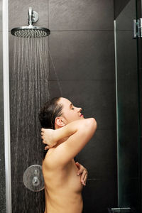 Shirtless woman taking shower in bathroom