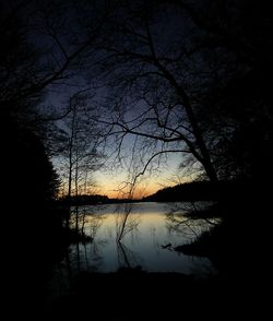 Silhouette bare trees by lake against sky during sunset