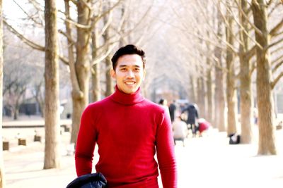 Portrait of smiling young man standing against bare trees during winter