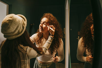 Young female friends helping each other in applying make-up at home