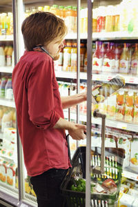 Side view of man answering mobile phone while shopping at freezer section in supermarket