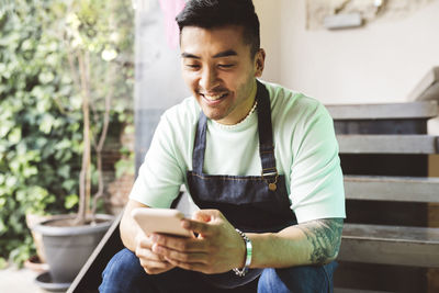 Happy man using mobile phone sitting on steps in coffee shop