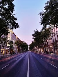 Road amidst trees and buildings against sky