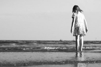 Full length rear view of girl standing at beach against clear sky