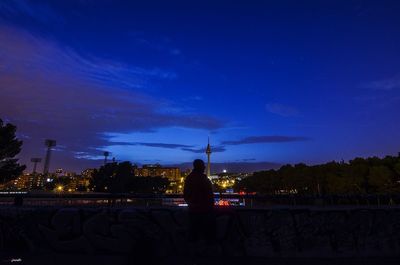 Silhouette of woman sitting on retaining wall against sky at night