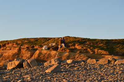 Rear view of man standing on rock against clear sky