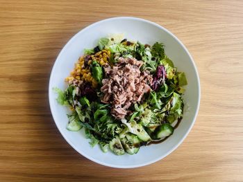 High angle view of a salad with greens and tuna in plate on wooden table