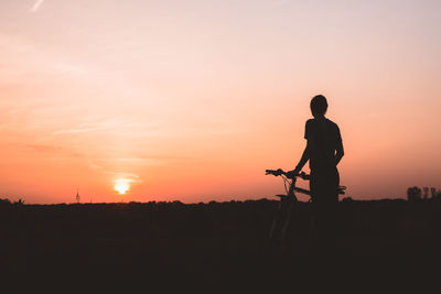 Silhouette man standing with bicycle on field against sky during sunset