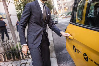 Midsection of businessman opening taxi door on city street