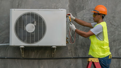 Side view of male technician repairing air conditioner on wall