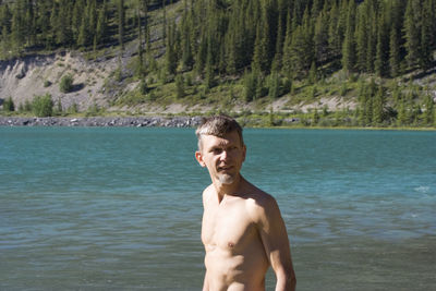 Shirtless man standing against river in forest on sunny day
