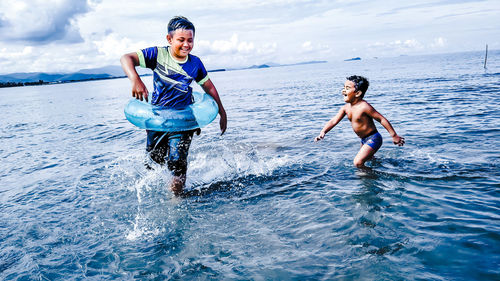 Siblings playing in sea against sky