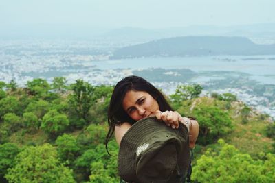 Portrait of young woman holding hat against landscape